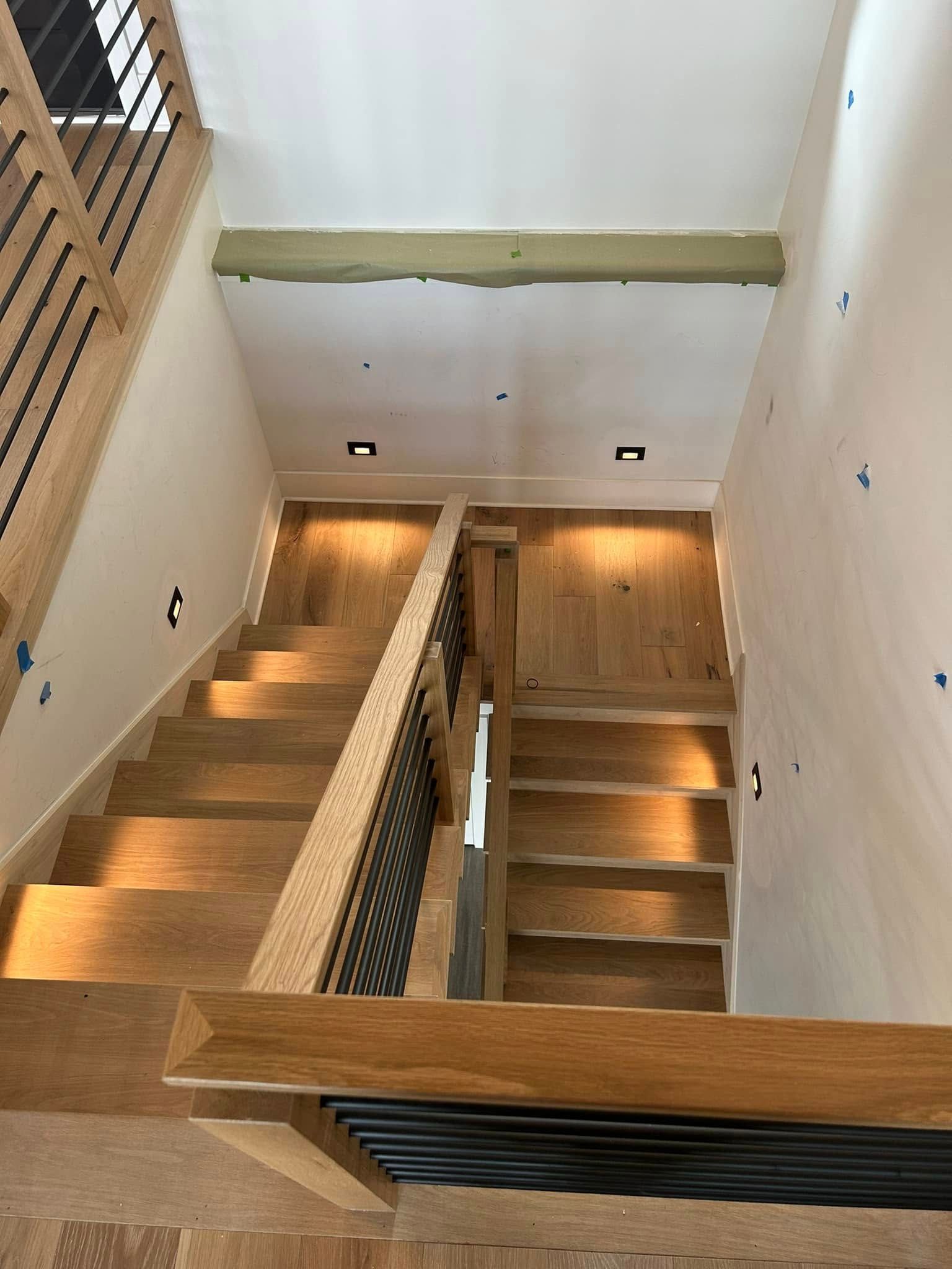 Modern stairwell with wood steps, white walls, and warm lighting, viewed from above