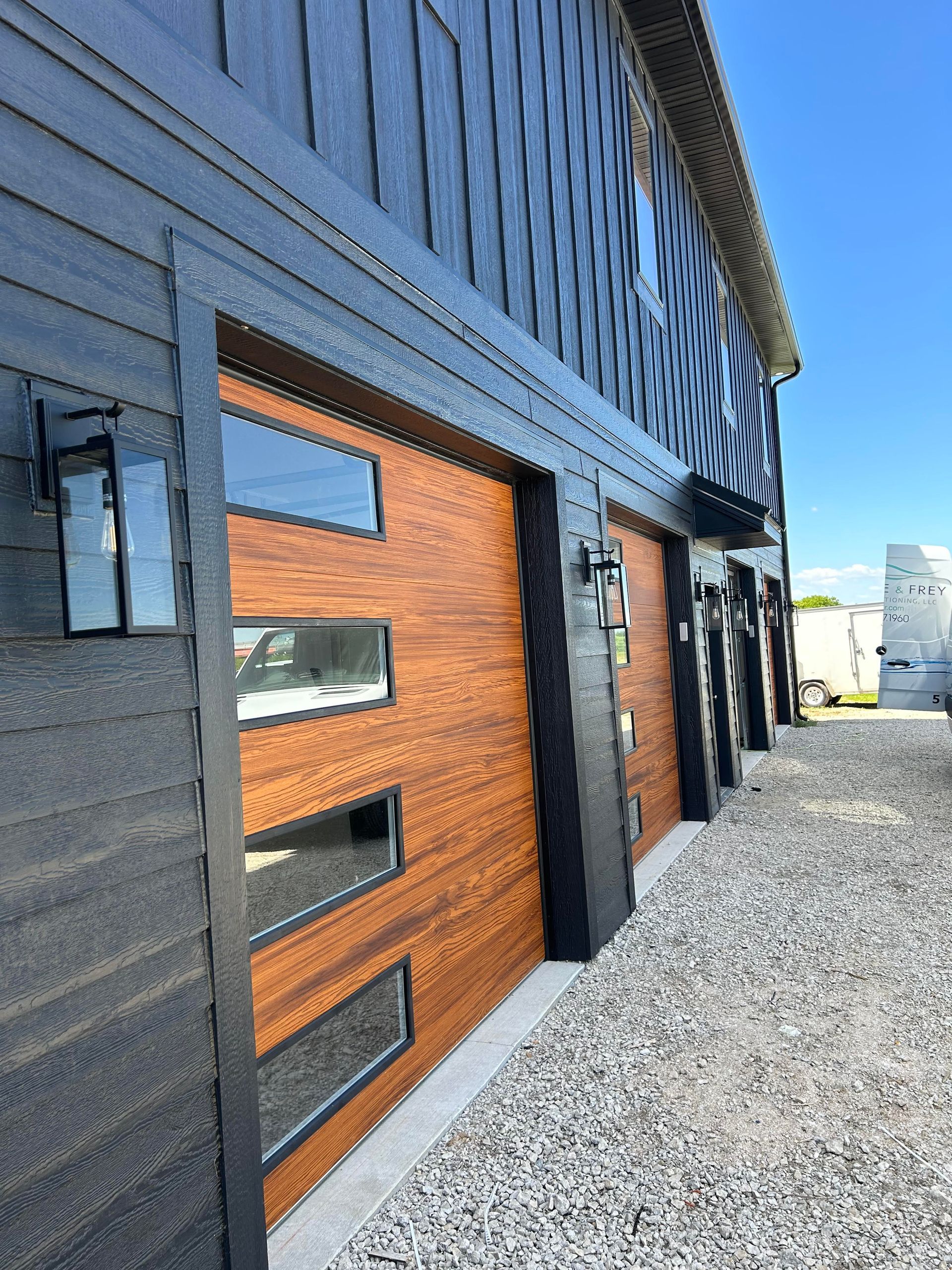 Black building exterior with wood door and narrow windows beside a gravel lot.