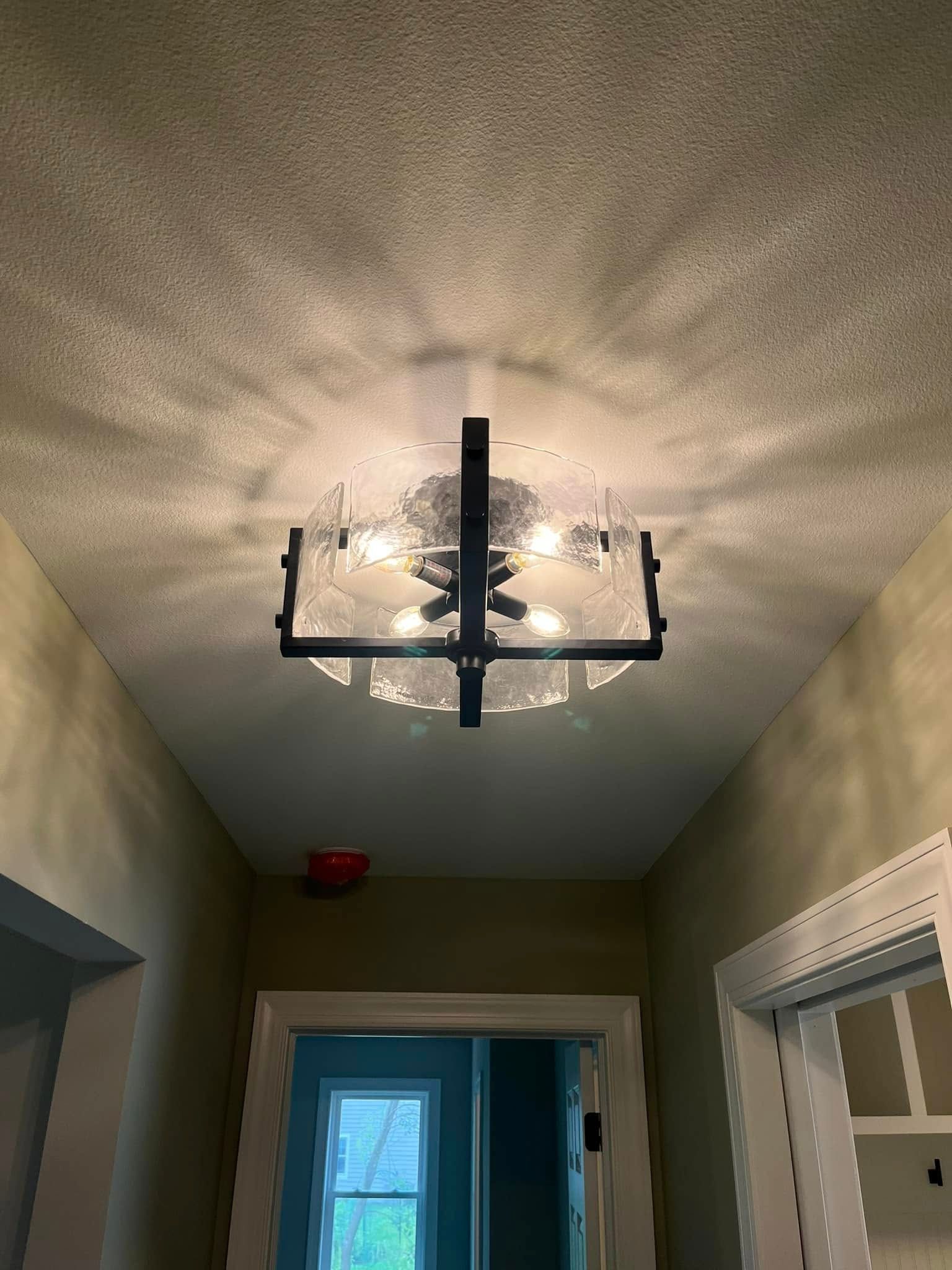 Black metal chandelier hanging from a textured beige hallway ceiling above a doorway.