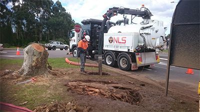 A man is standing next to a vacuum truck that says nls on the side.