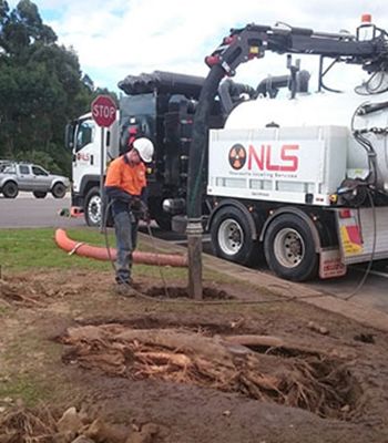 A man is standing in front of a vacuum truck that says nls on the side.