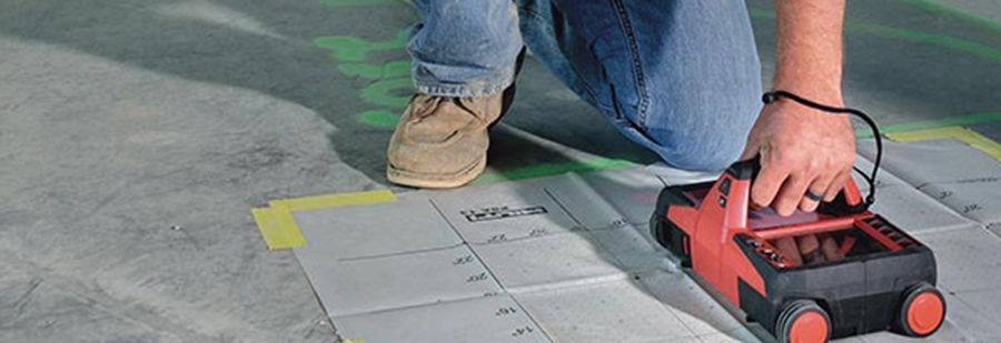 A man is kneeling down while using a machine on the ground.
