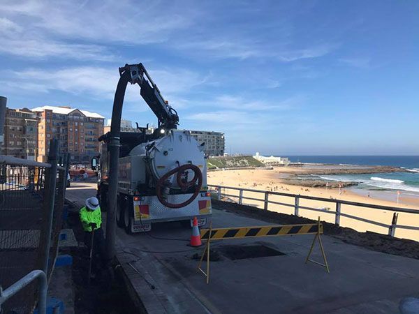 A vacuum truck is parked on the side of the road next to a beach.