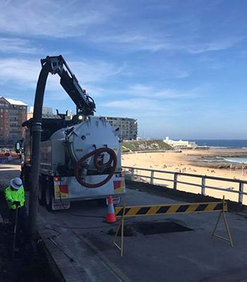 A vacuum truck is parked on the side of the road next to a beach.