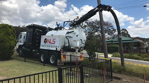 A vacuum truck is cleaning a power pole in a yard.