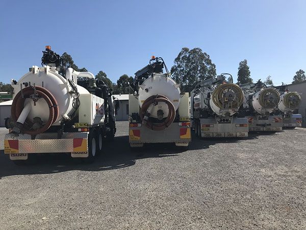 A row of vacuum trucks are parked in a gravel lot.