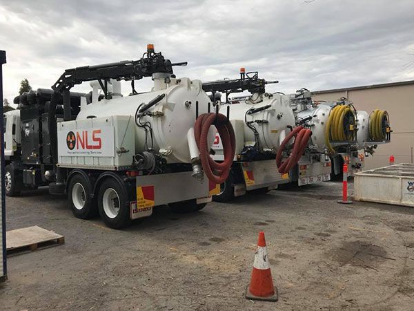 A row of vacuum trucks are parked in a parking lot.
