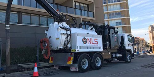 A vacuum truck is parked on the side of the road in front of a building.
