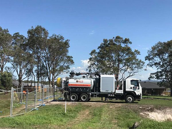 A vacuum truck is parked in a grassy field next to a fence.