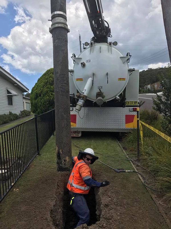 A man is standing in a hole next to a vacuum truck.