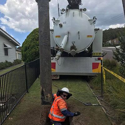 A man is digging a hole in front of a vacuum truck.