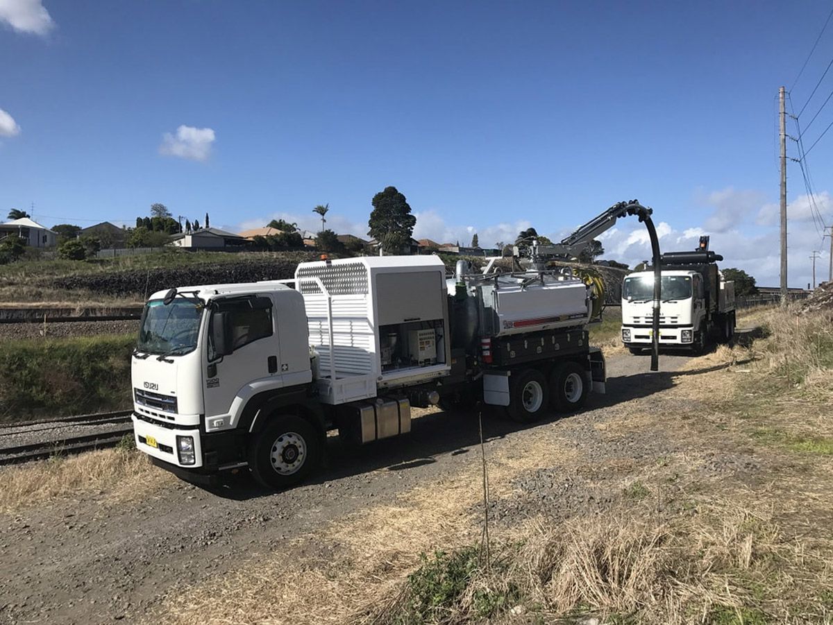 Two trucks are parked next to each other on a dirt road.