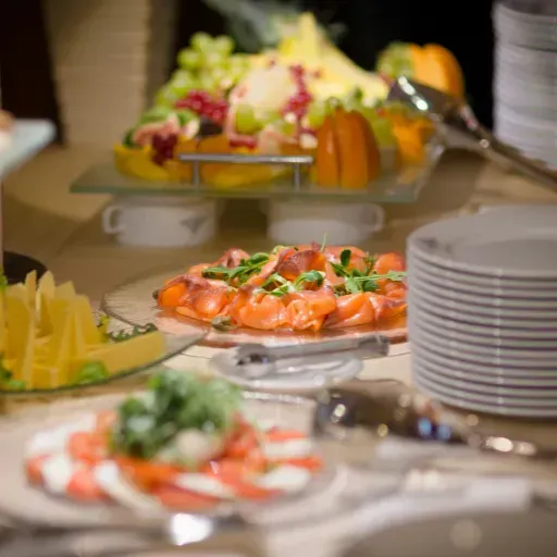 Buffettafel met schalen garnalen, fruitschalen en gestapelde witte borden.
