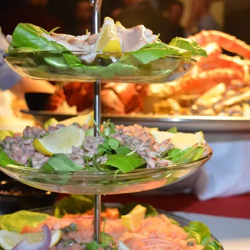 Een etagère met drie etages vol hapjes, salade en citroenpartjes op een buffet.