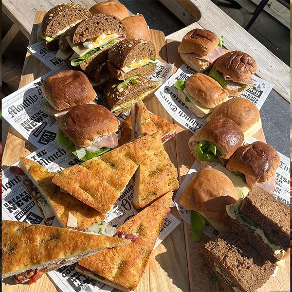 Diverse sandwiches en geroosterd platbrood op met krantenpapier beklede schalen in de buitenlucht.