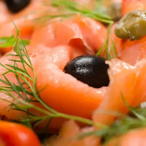 Gerookte zalm met zwarte olijven en dille op een bord.