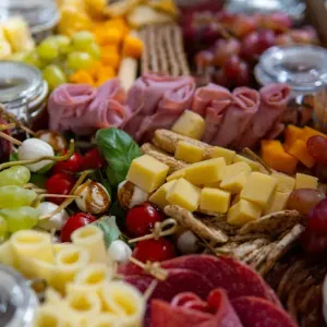 Een charcuterieplank met kazen, vleeswaren, druiven, olijven en crackers, uitgestald op tafel.