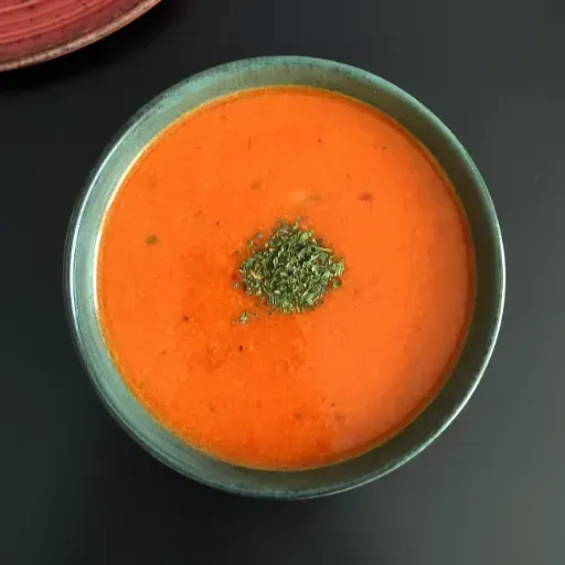 Een kom romige sinaasappelsoep met kruiden op een donkere tafel.