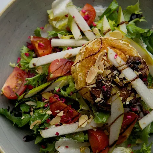 Verse salade met bladgroenten, tomaten, perenschijfjes, amandelen en een topping van ronde kaas.