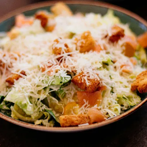 Caesarsalade met croutons en geraspte kaas in een zwarte kom.