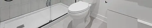 A modern bathroom featuring a white toilet next to a glass-enclosed walk-in shower with light grey tiled walls.