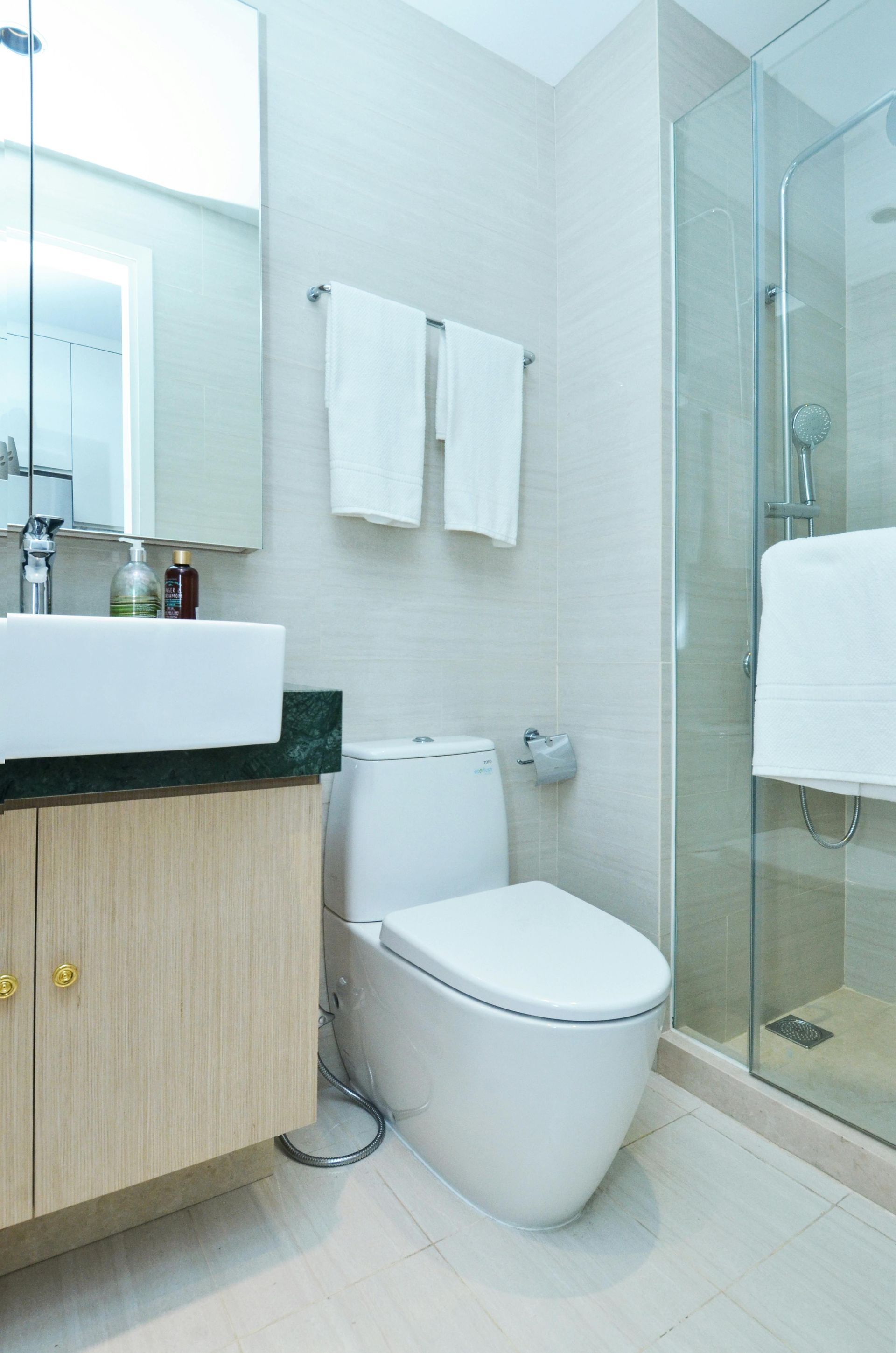 Modern bathroom with a toilet, sink, and glass shower. White towels hang on a rack above the toilet.