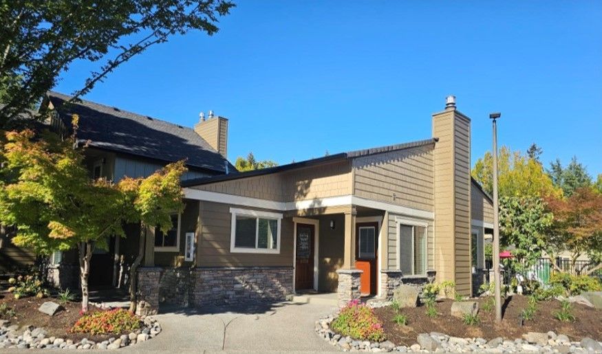Modern house exterior with stone and wood siding, front garden, and blue sky