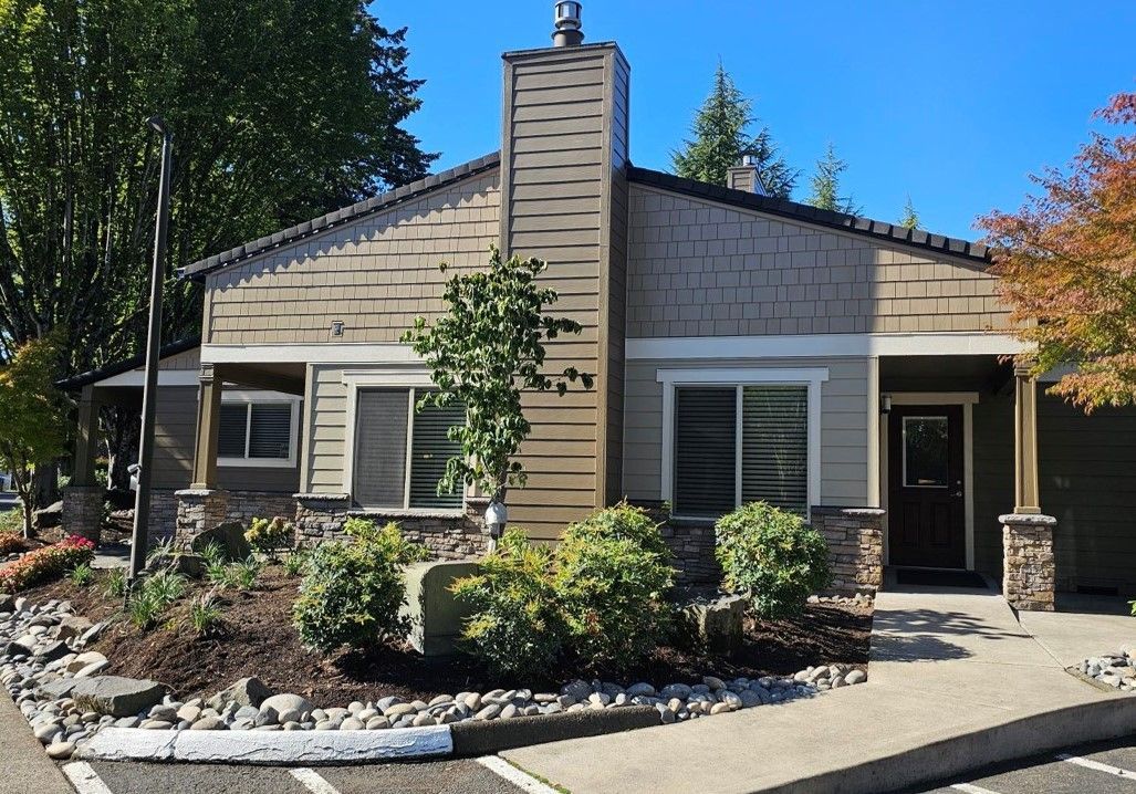 Single-story house with a front porch, central chimney, and landscaped front yard in daylight