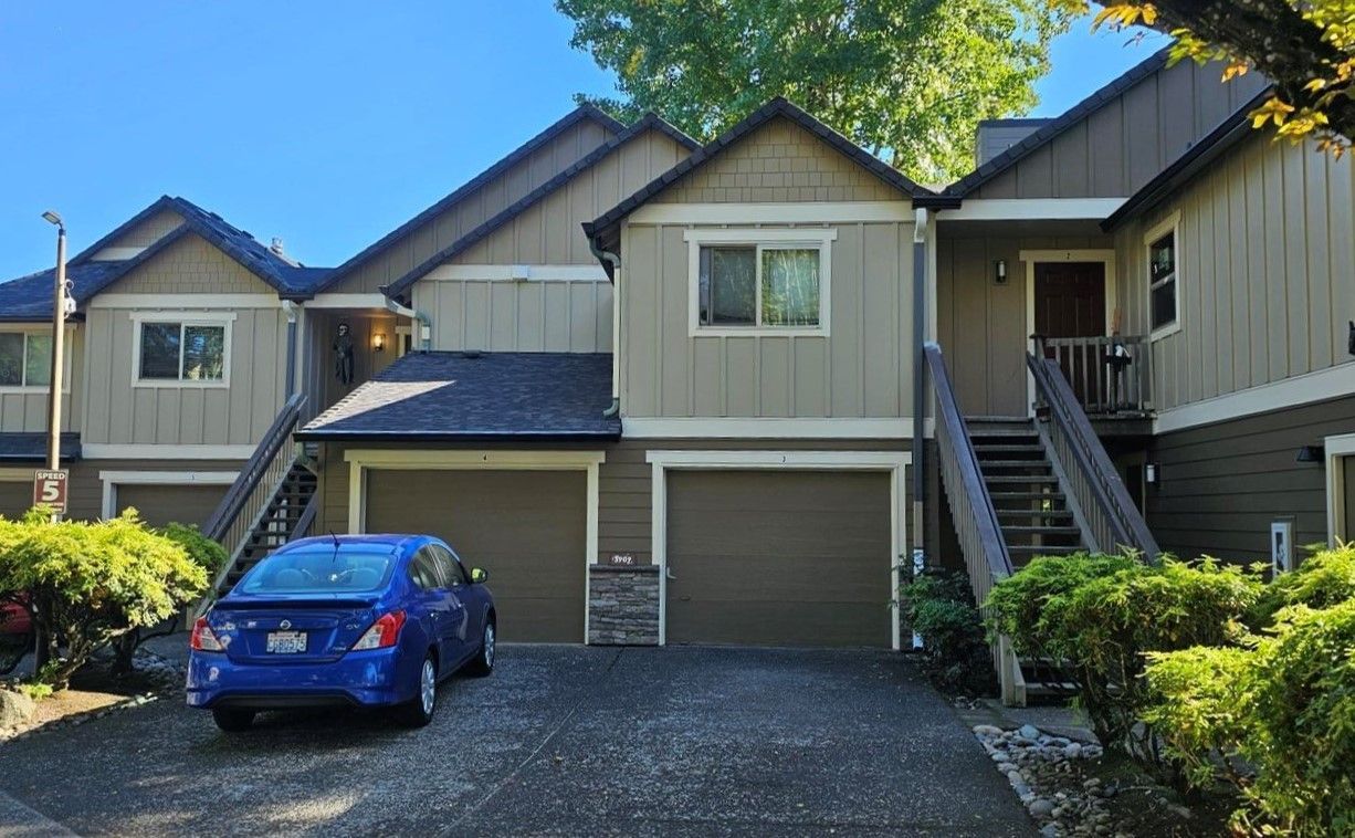 Row of townhouses with garage doors, blue car parked out front, and exterior stairs on the right.