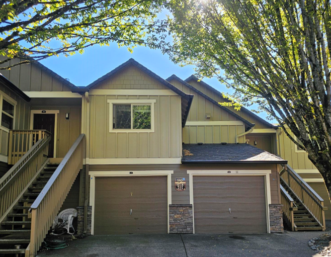 Townhouse exterior with two garage doors, beige siding, and trees framing the front entrance