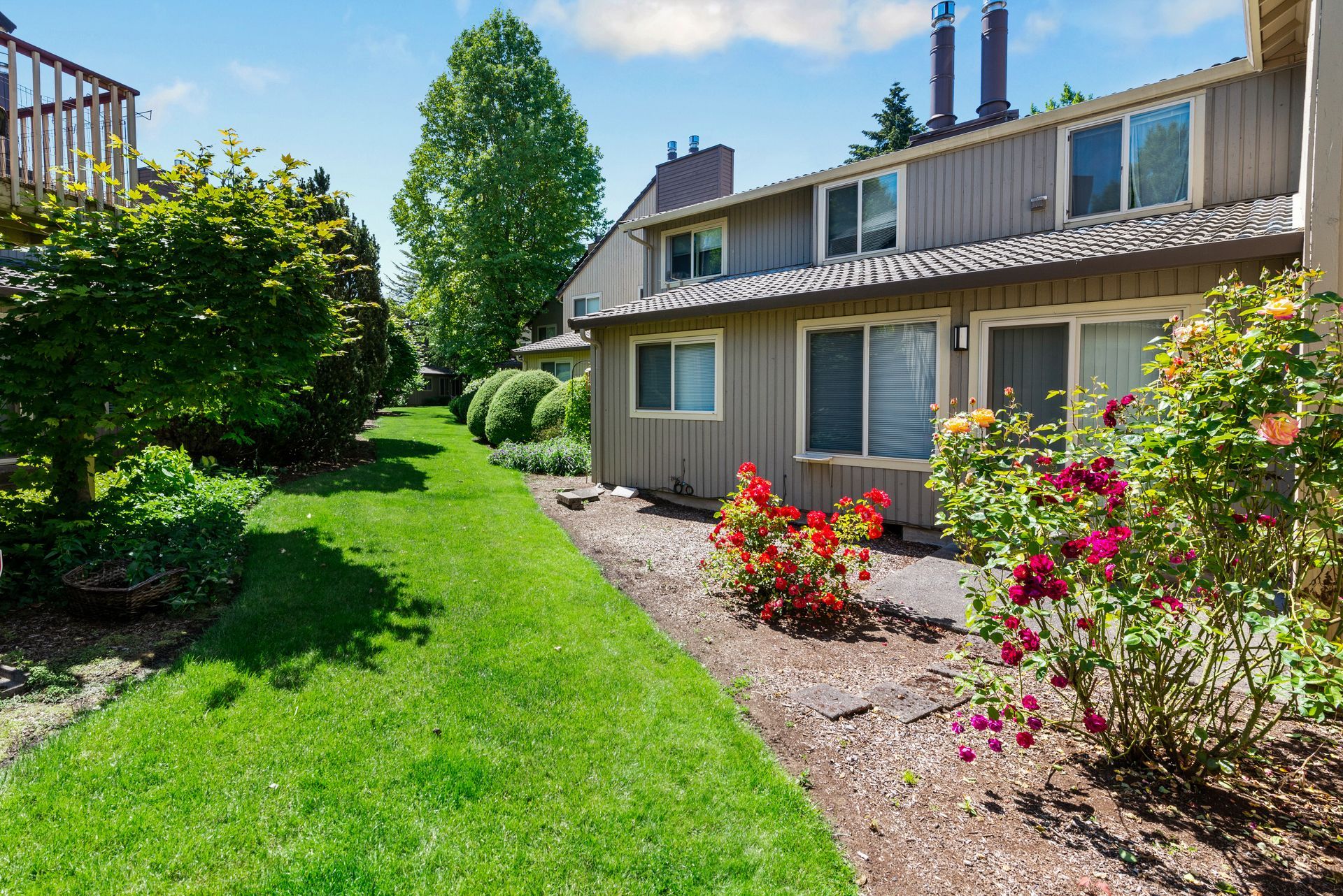 Sunny suburban townhouse with green lawn, flowerbeds, and a beige two-story exterior