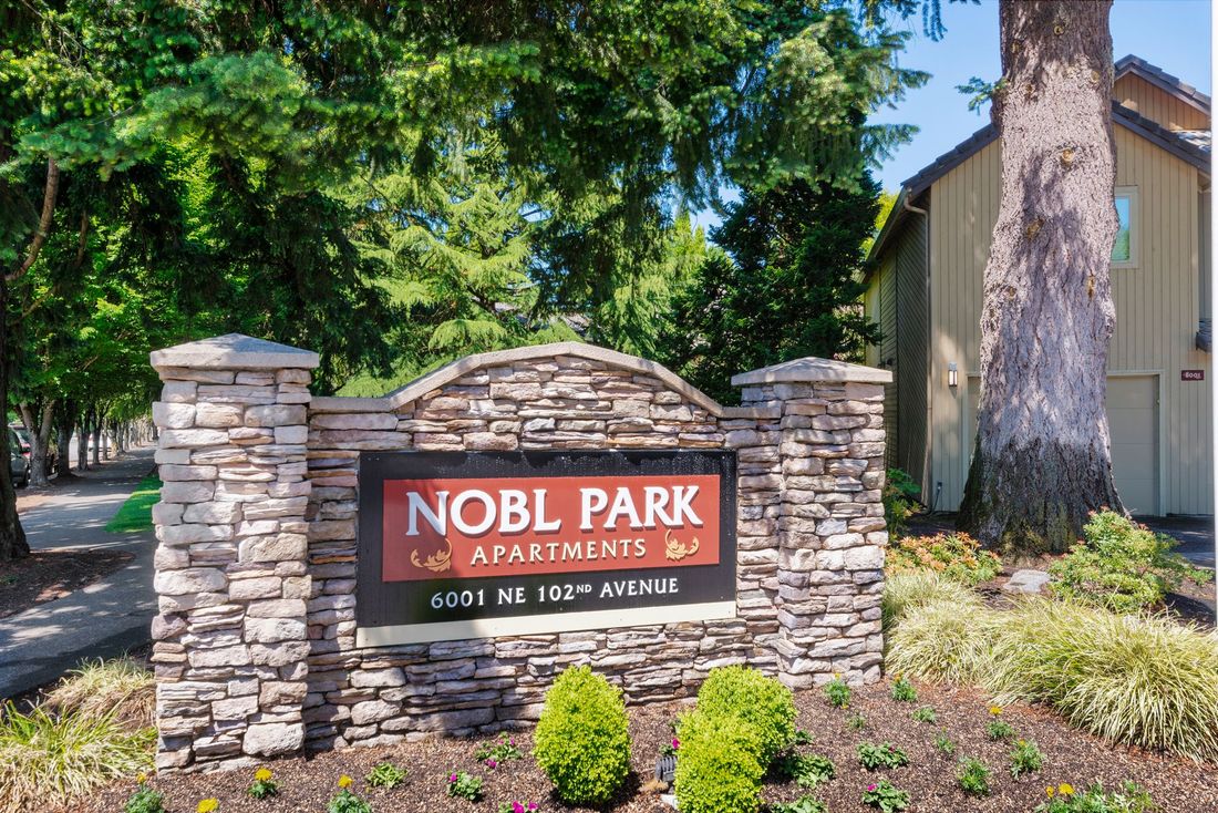 Nobl Park Apartments entrance sign on a stone wall amid trees and landscaping