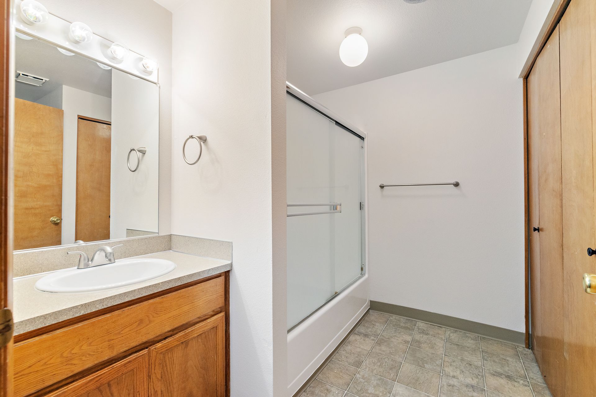 Bright bathroom with vanity, mirror, glass shower, towel bar, and wood door.
