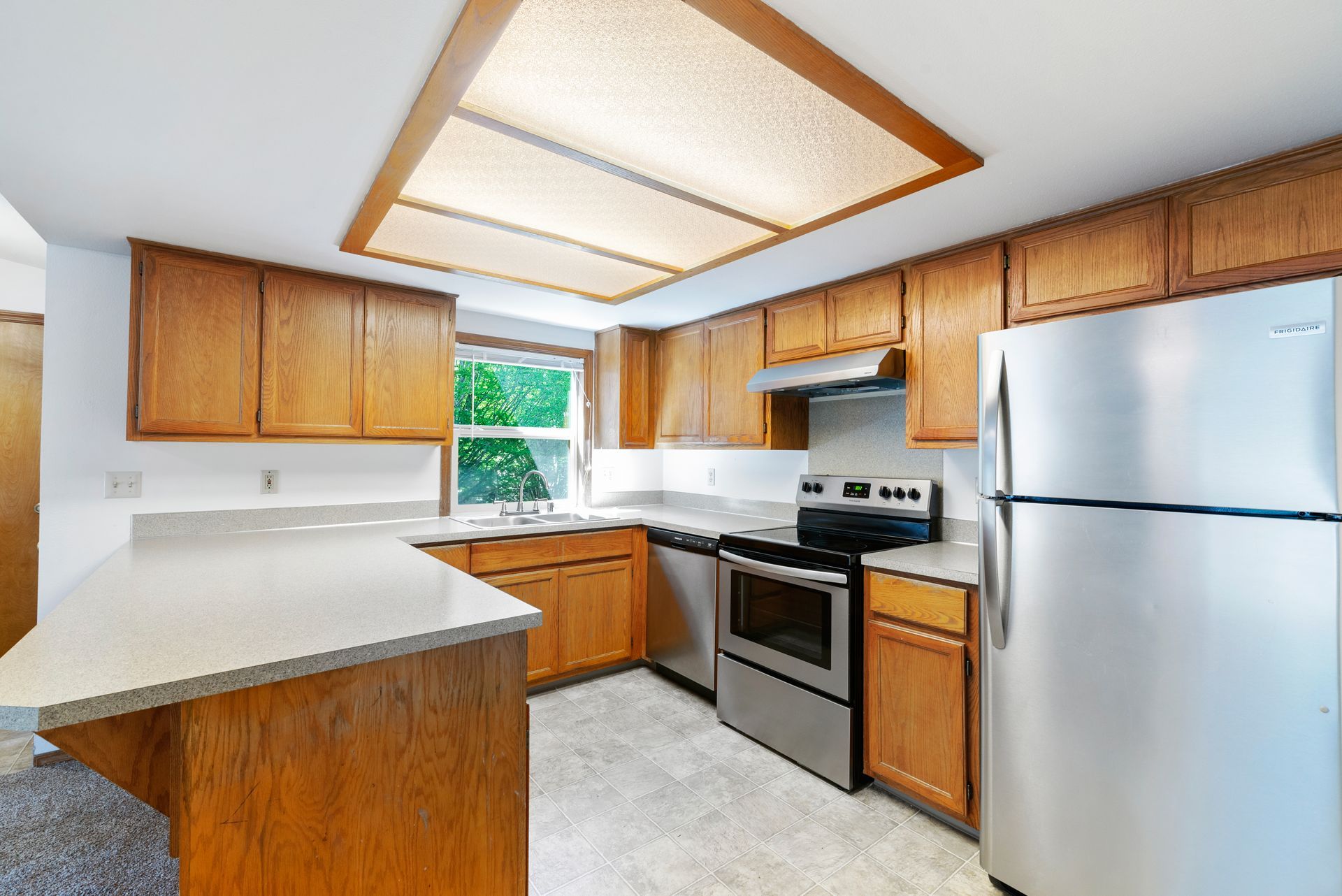 Bright kitchen with wood cabinets, white countertops, stainless stove and fridge, and skylight ceiling.
