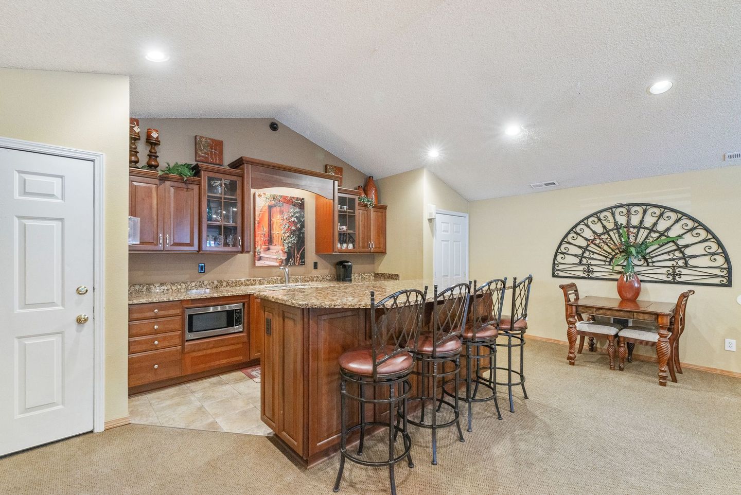 Open-concept kitchen and dining area with wood cabinets, island stools, and large wall clock.