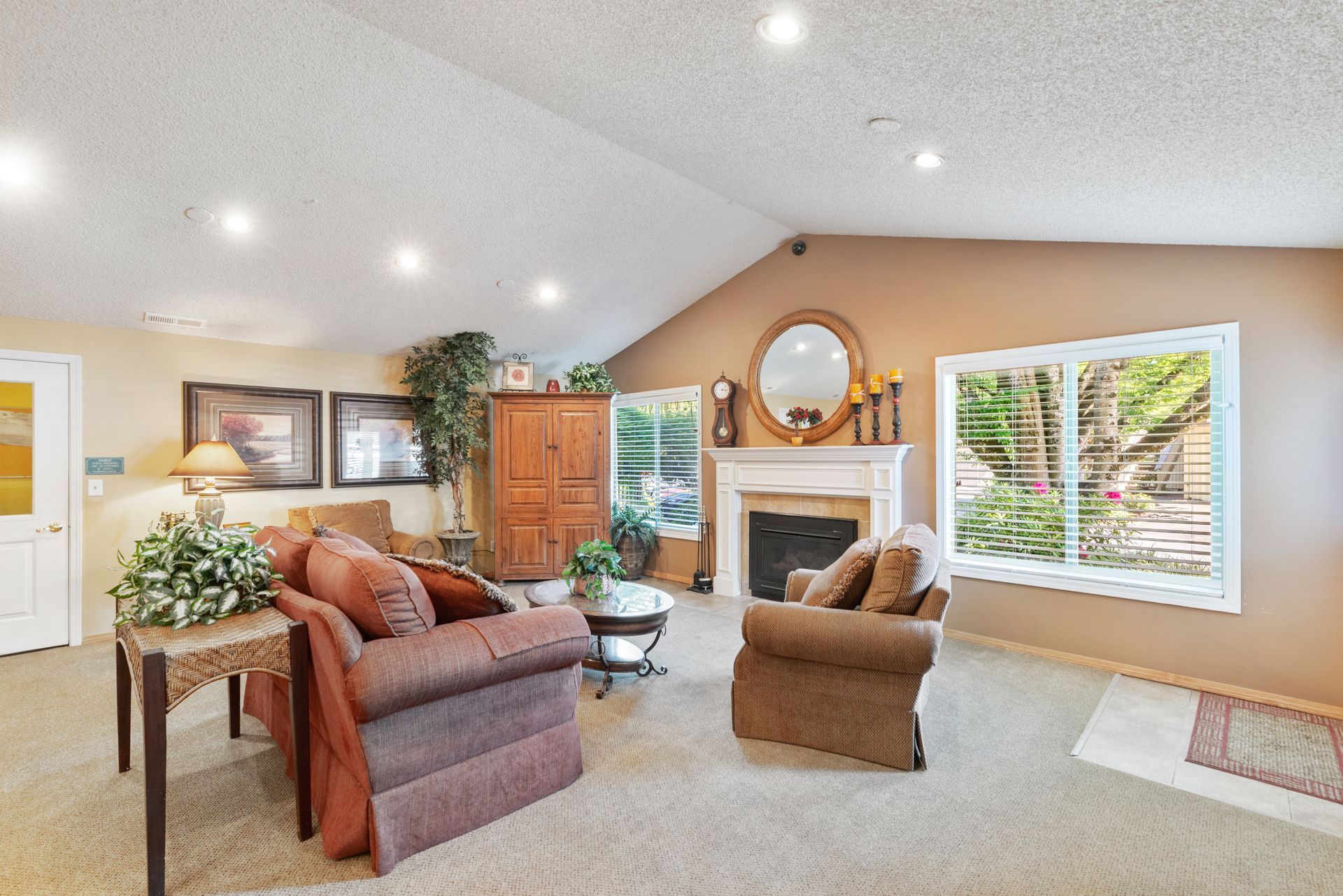 Bright living room with fireplace, tan recliners, wood cabinet, and large window blinds