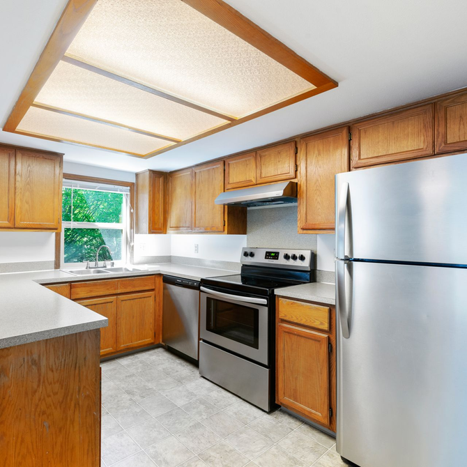 Bright kitchen with wood cabinets, stainless steel appliances, white countertops, and a window over the sink.