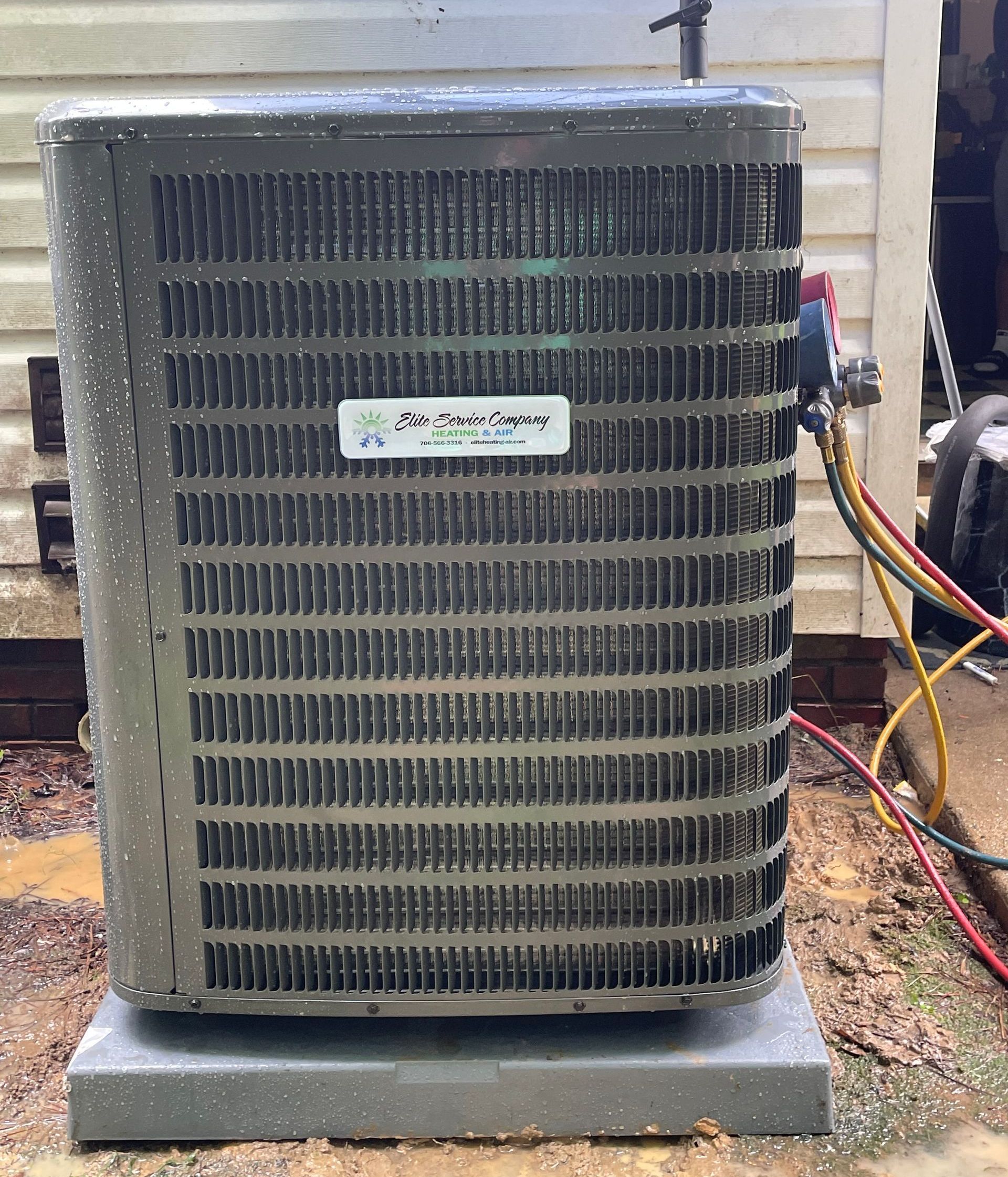 A dirty air conditioner is sitting on top of a concrete base in front of a house.
