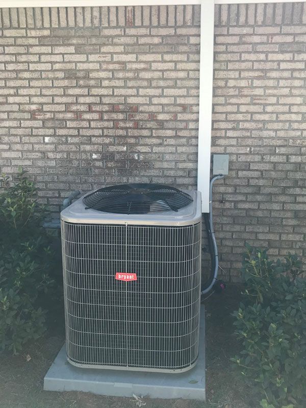 A large air conditioner is sitting in front of a brick wall.