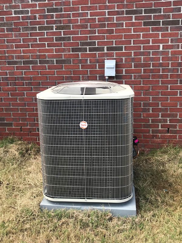 A large air conditioner is sitting in front of a brick wall.