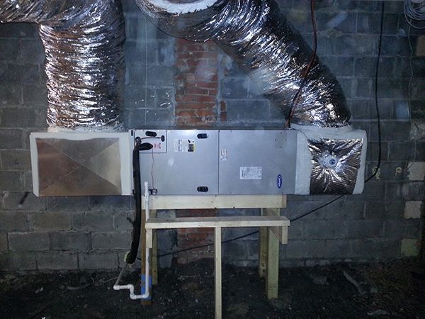 A ventilation system is installed in a basement next to a brick wall.