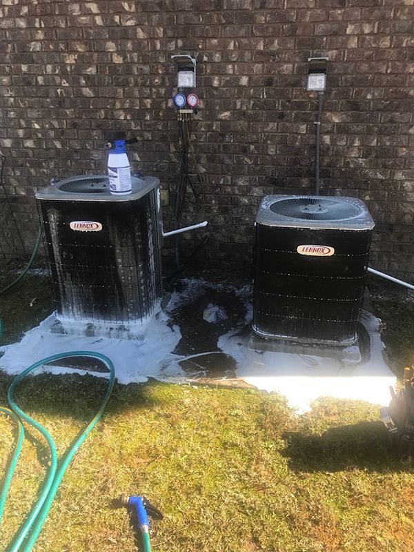 Two air conditioners are being cleaned outside of a brick building.