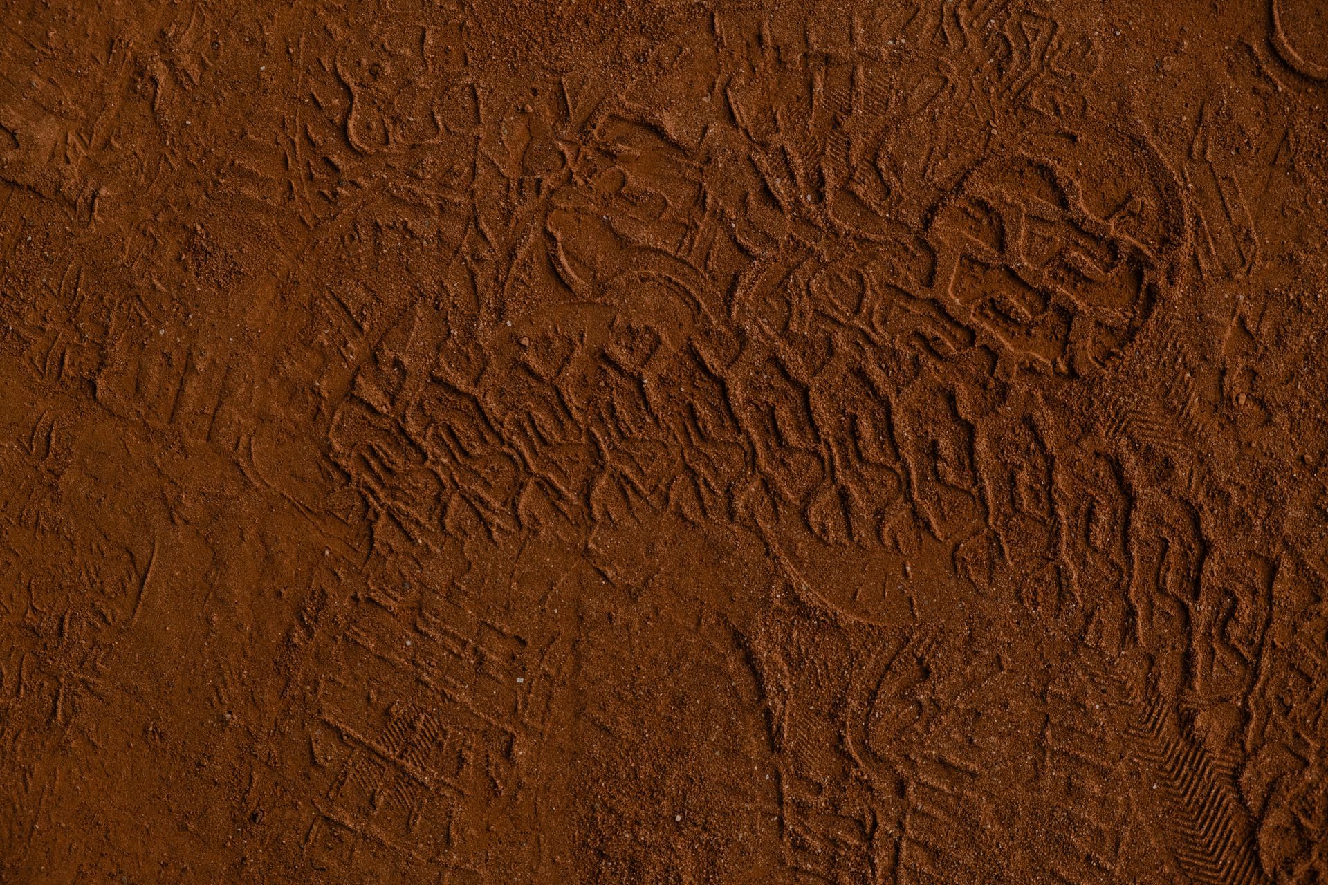 Footprint imprints in reddish-brown sand, showing the tread pattern of a boot.