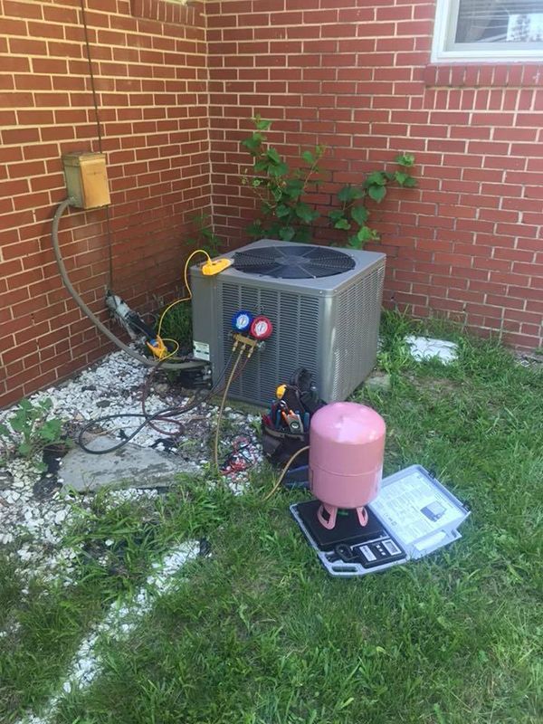An air conditioner is being installed in the backyard of a brick house.