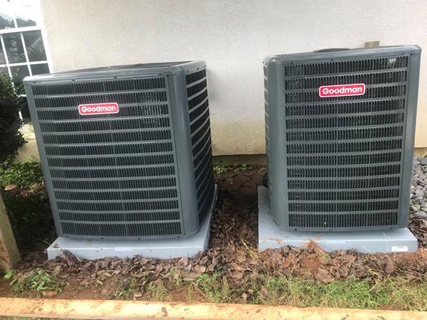 Two air conditioners are sitting next to each other on the side of a house.