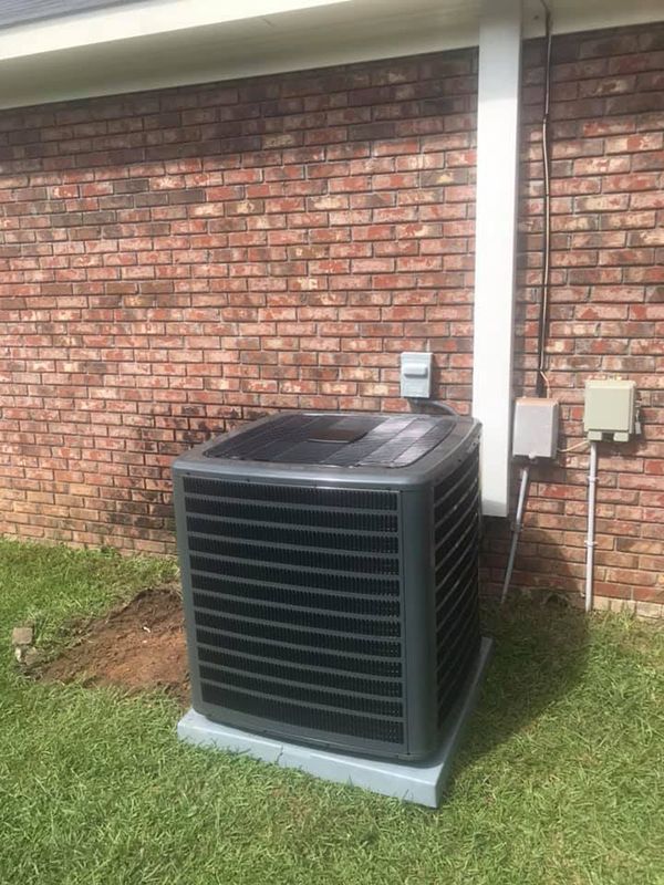 A large air conditioner is sitting on the side of a brick building.