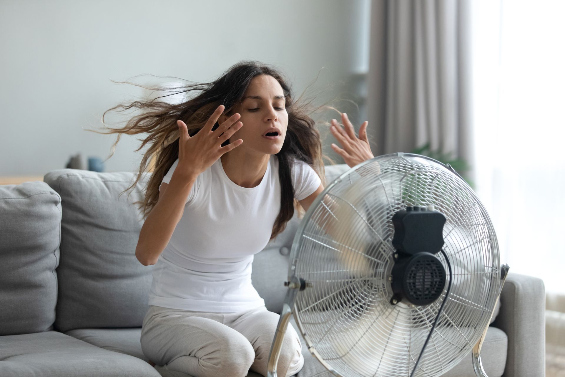 A woman is sitting on a couch in front of a fan.