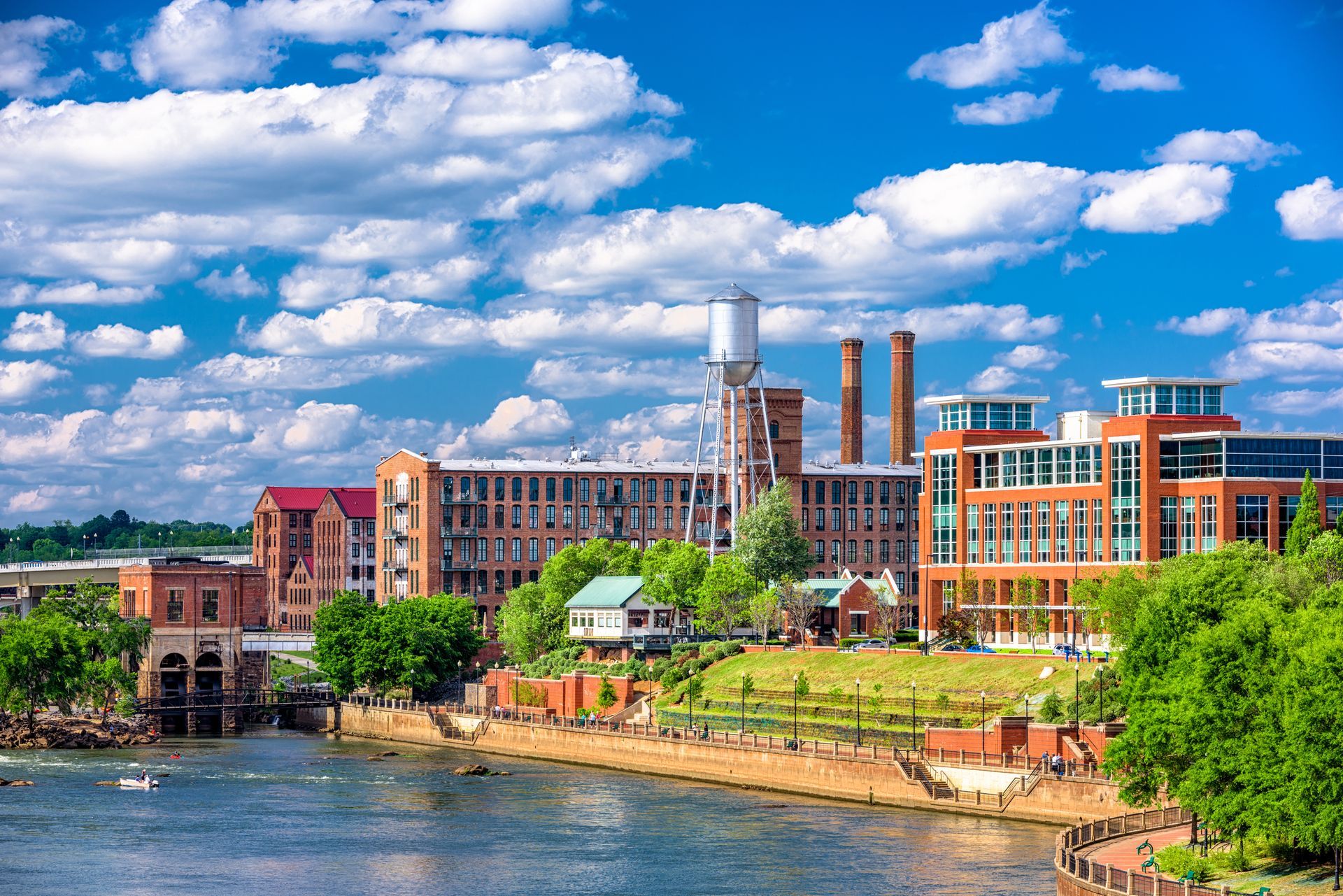 A city with a river , buildings , trees and a blue sky with clouds.