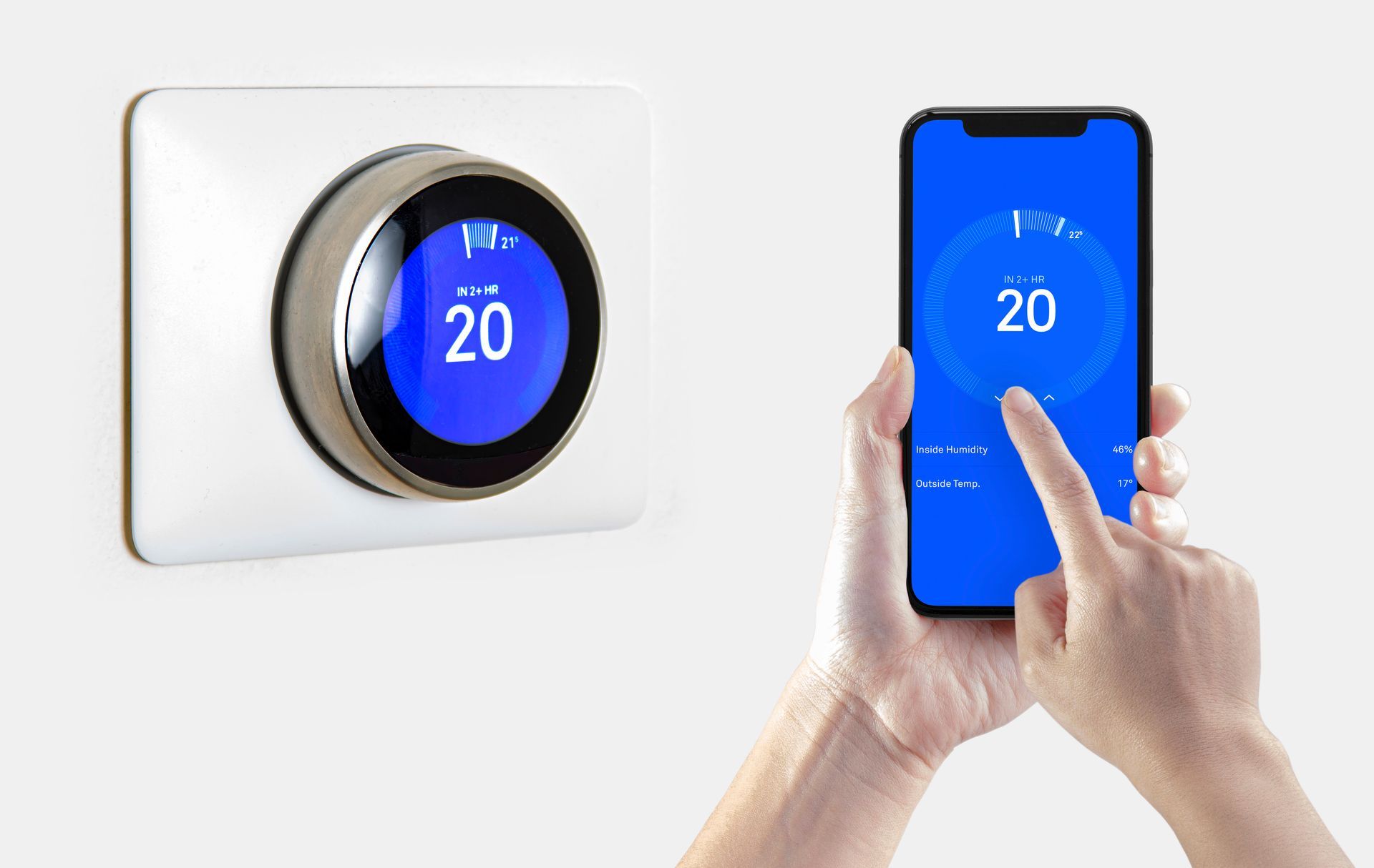 Smart thermostat and smartphone displaying temperature of 20 degrees. Hand touching phone screen.
