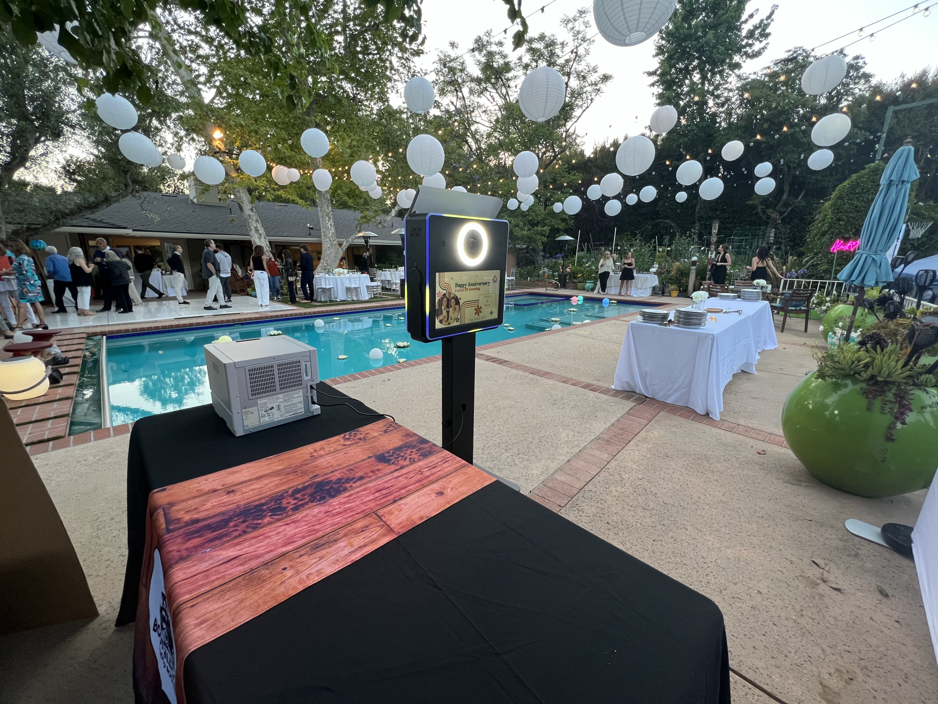 A photo booth is sitting on a table in front of a pool.